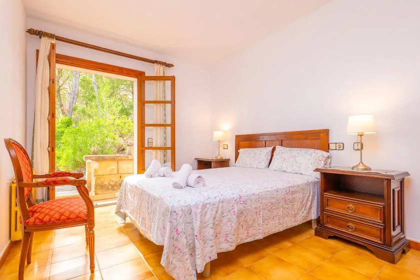 A bedroom with a double bed and an open doorway overlooking greenery.