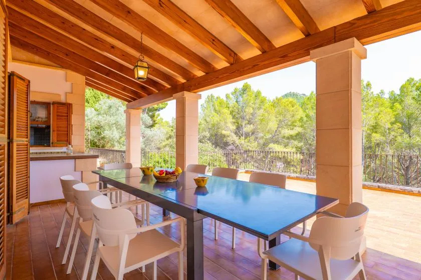 A covered outdoor dining area with a long table and chairs overlooks a wooded landscape.