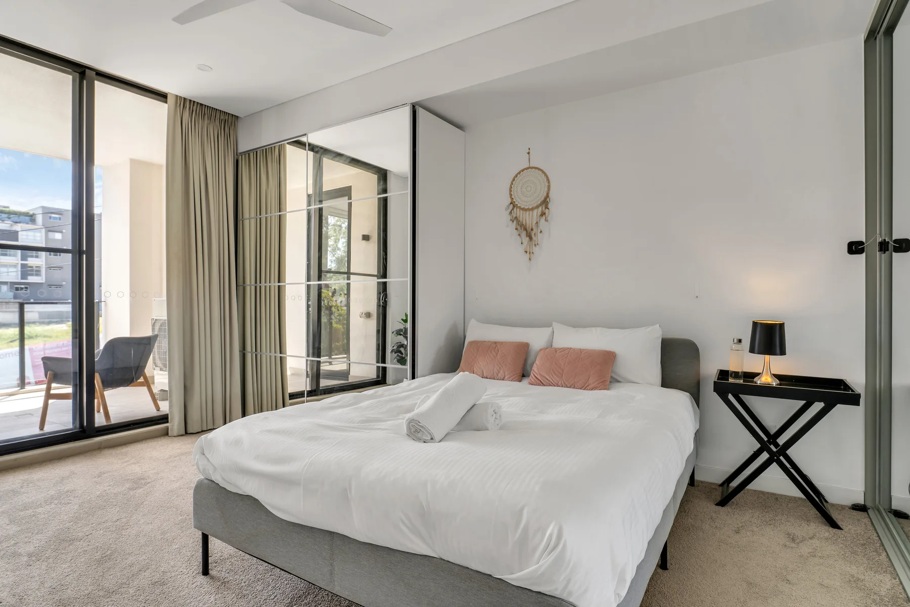 A bright bedroom with a neatly made bed and glass doors opening to a balcony.