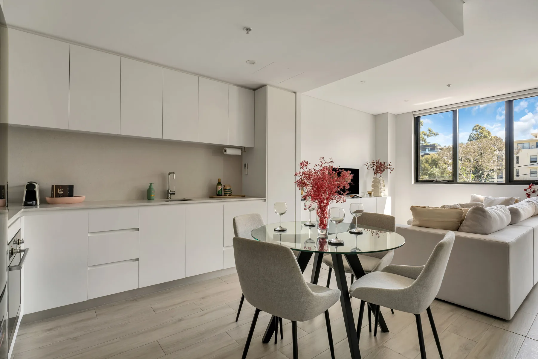 A bright open-plan kitchen and dining area with a living space by large windows.