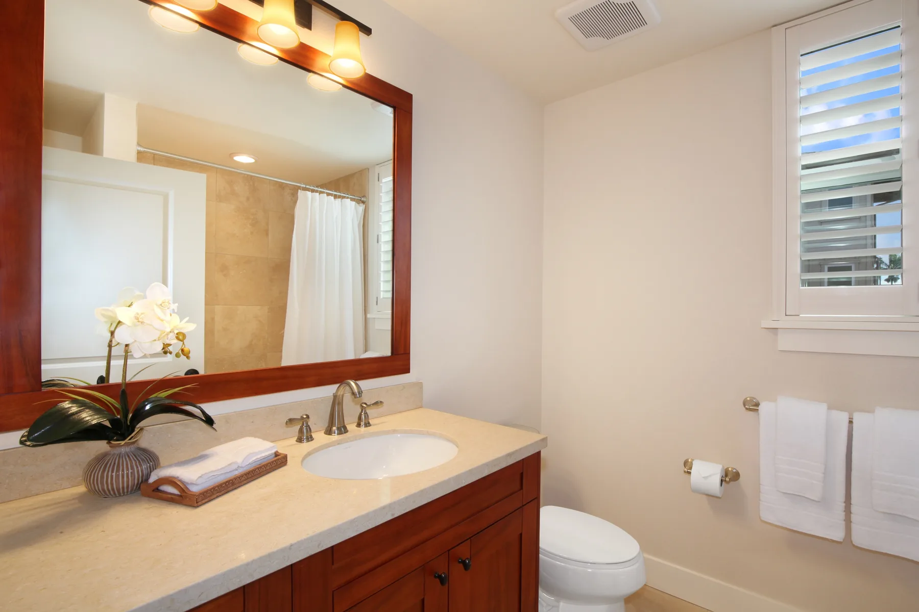Un tocador de baño con lavabo y espejo junto a un inodoro y una ventana.