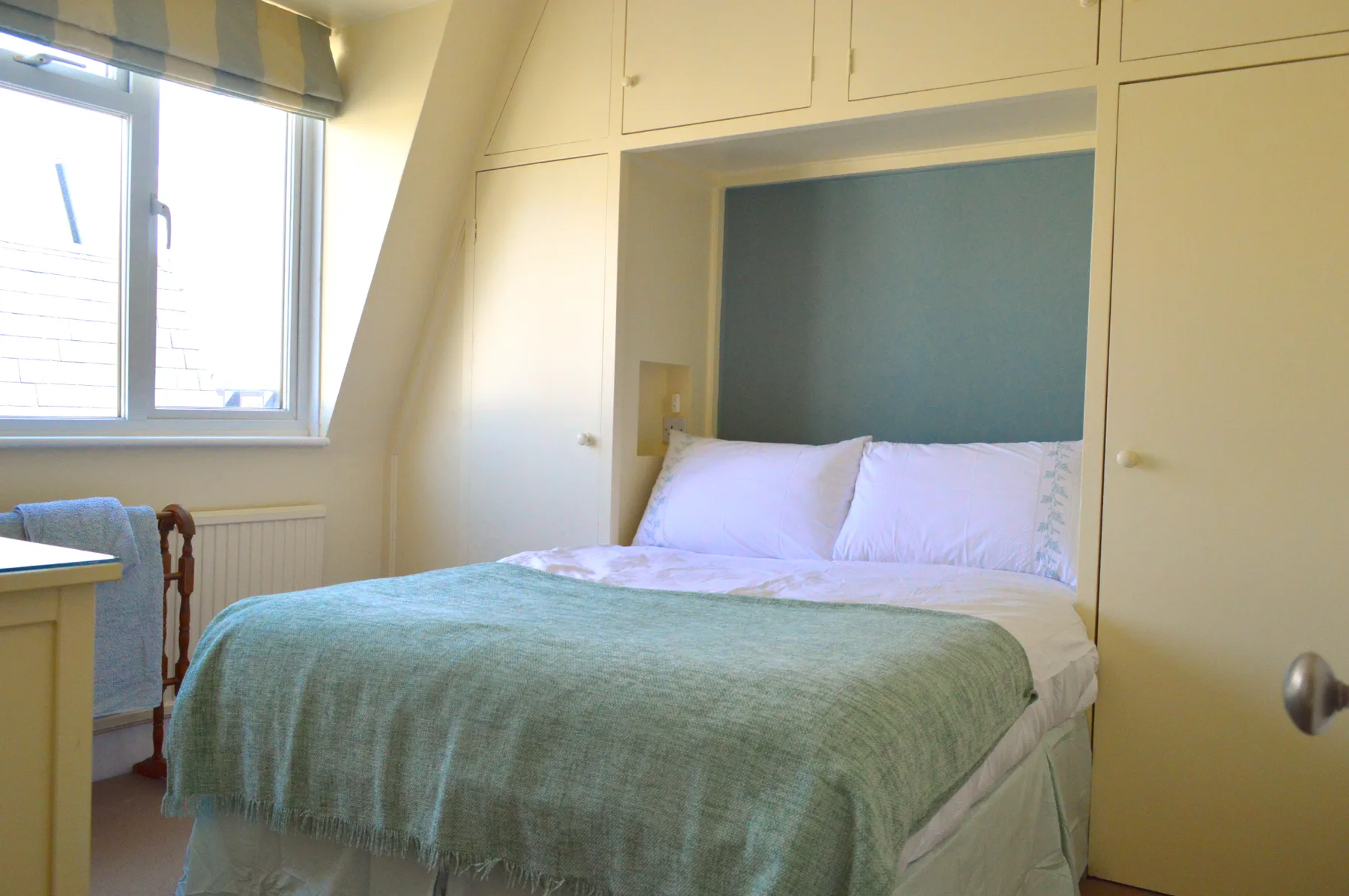 Dormitorio con una cama bajo armarios empotrados y junto a una ventana.