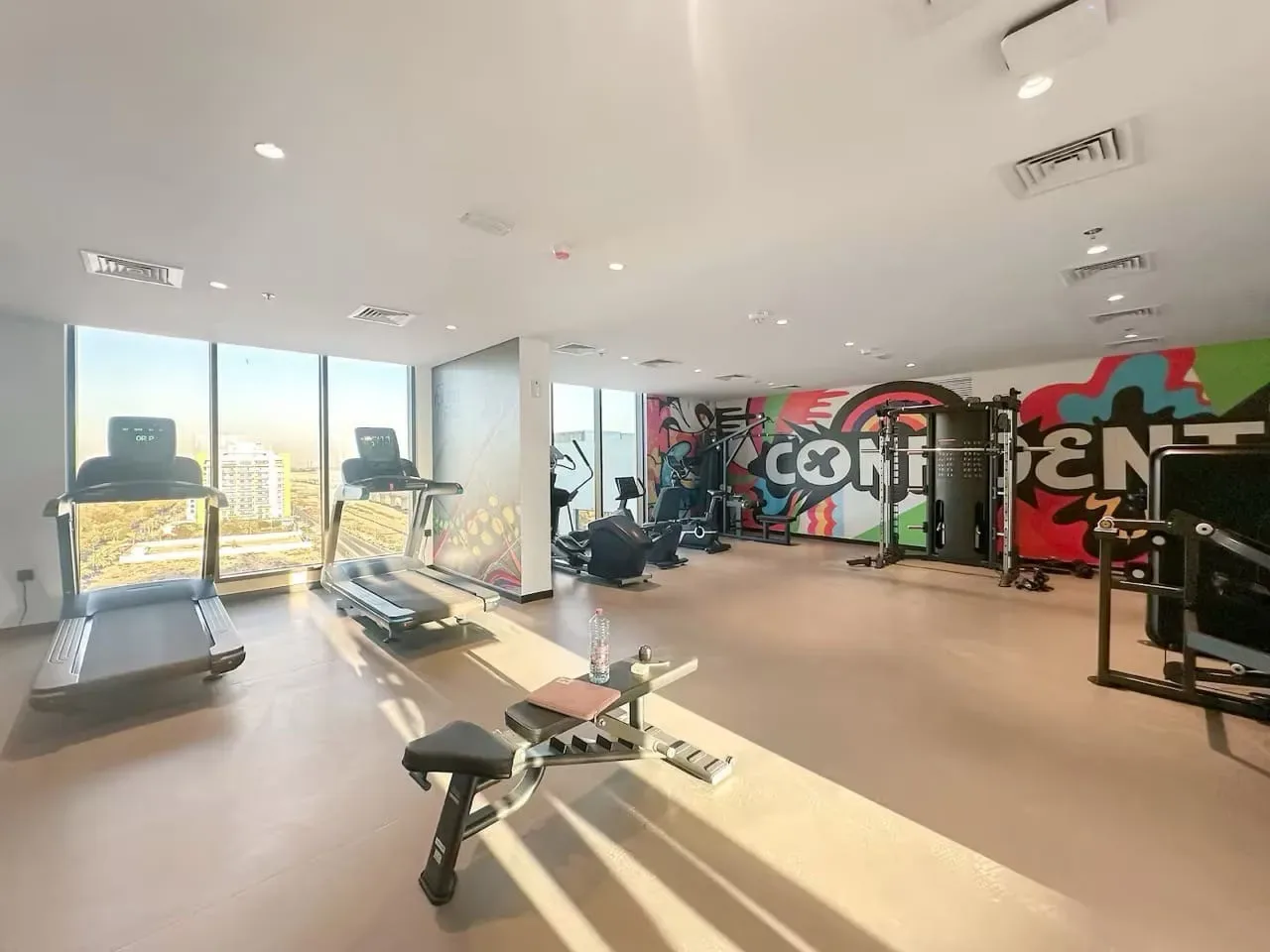 Un gimnasio con cintas de correr, equipos de ejercicio y un mural colorido en la pared del fondo.
