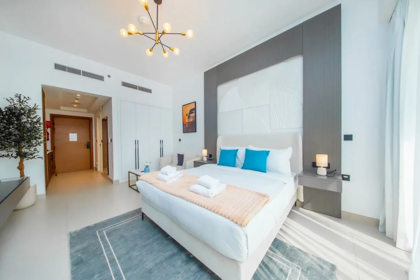 Un dormitorio luminoso con una cama, almohadas azules y una mesita de noche.