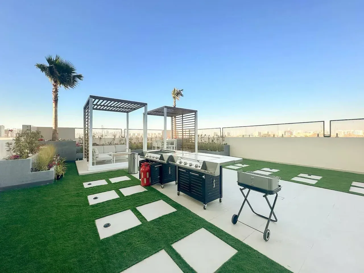 Una terraza en la azotea con césped artificial, asientos al aire libre y pérgolas bajo un cielo despejado.