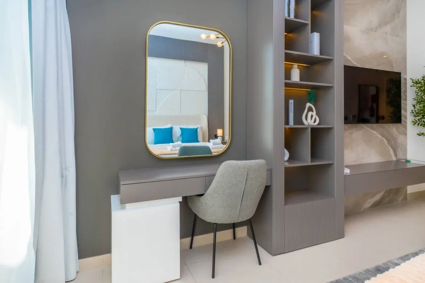 Zona de tocador en un dormitorio moderno, con espejo, asiento y estanterías integradas.