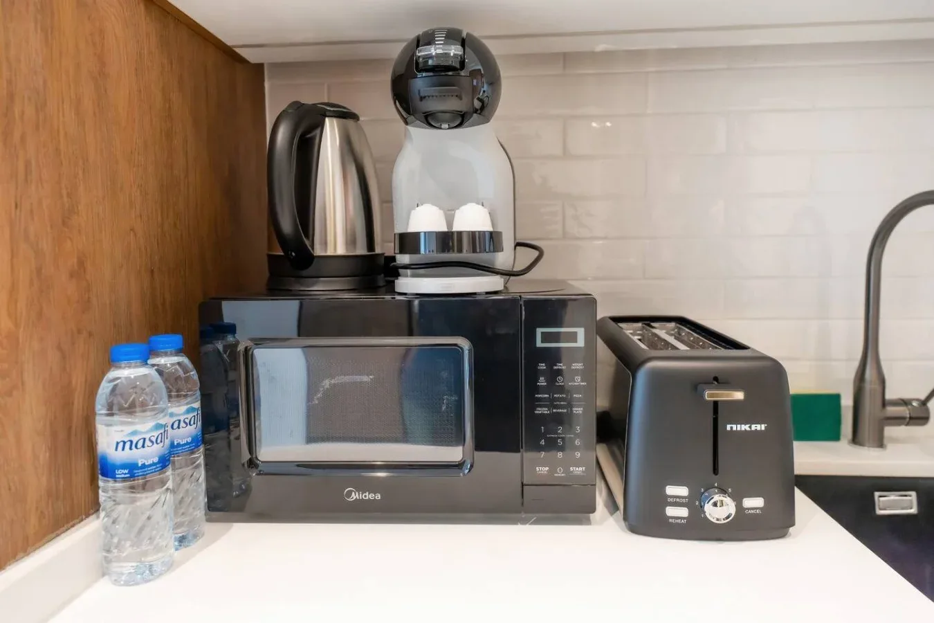 Una encimera de cocina con microondas, hervidor, cafetera y tostadora.