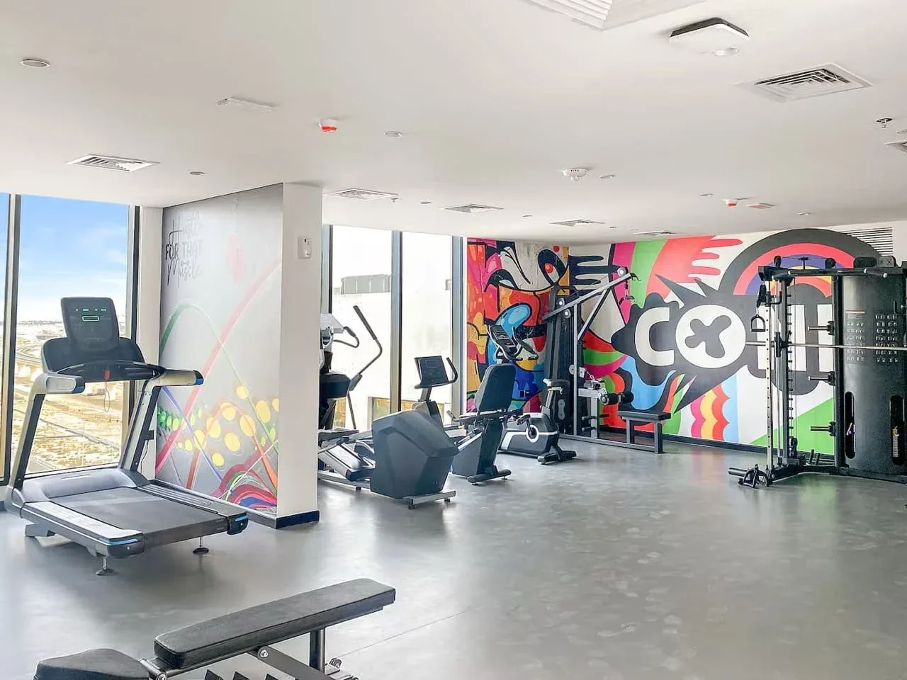 Un gimnasio con cintas de correr y equipo de ejercicio junto a un mural colorido.