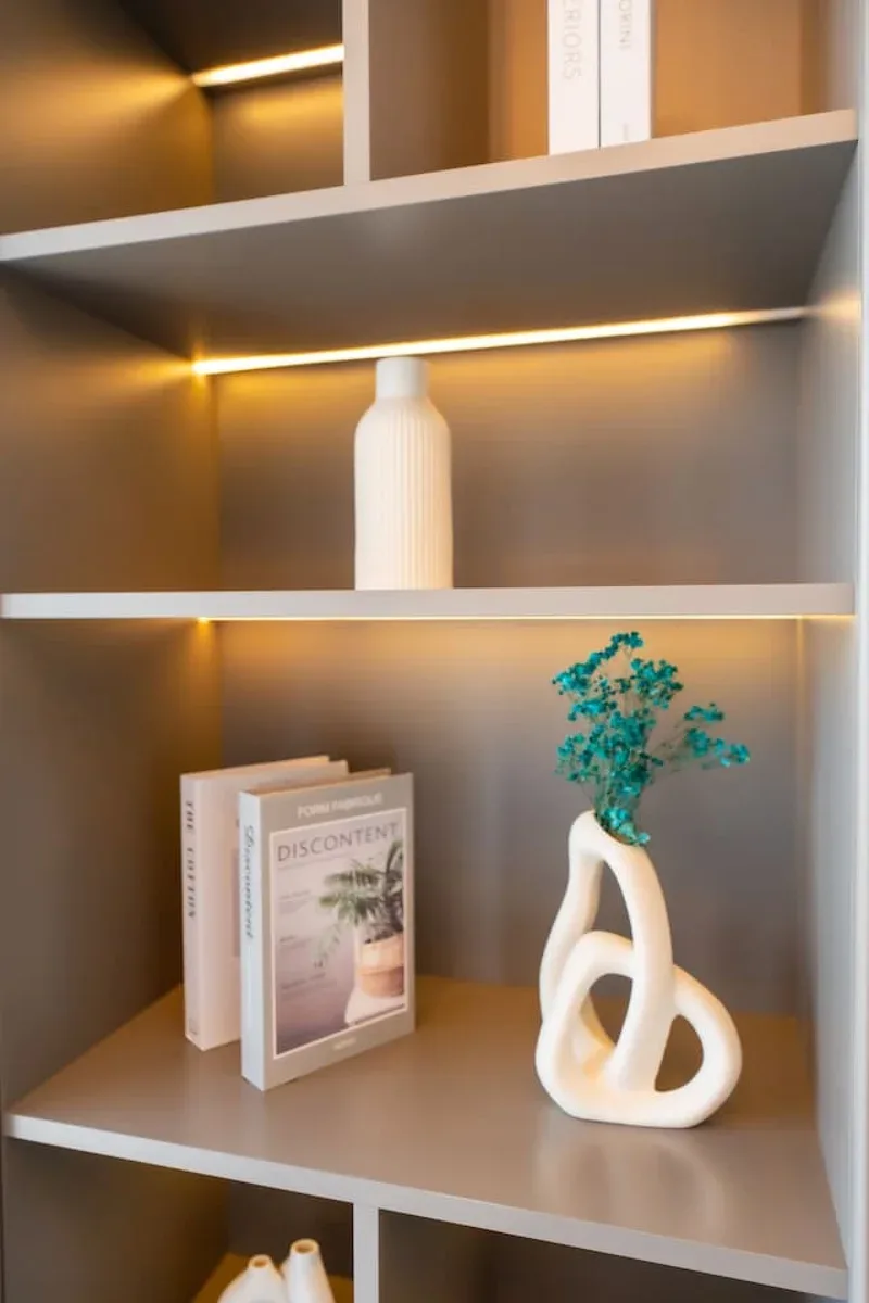Estantes decorativos exhiben libros, jarrones blancos y un pequeño arreglo de vegetación.