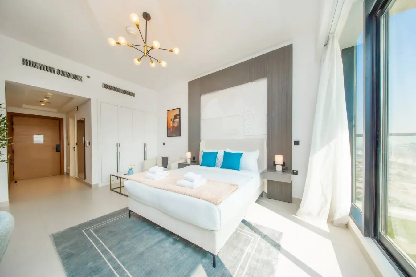 Un dormitorio luminoso con una cama blanca junto a ventanales.