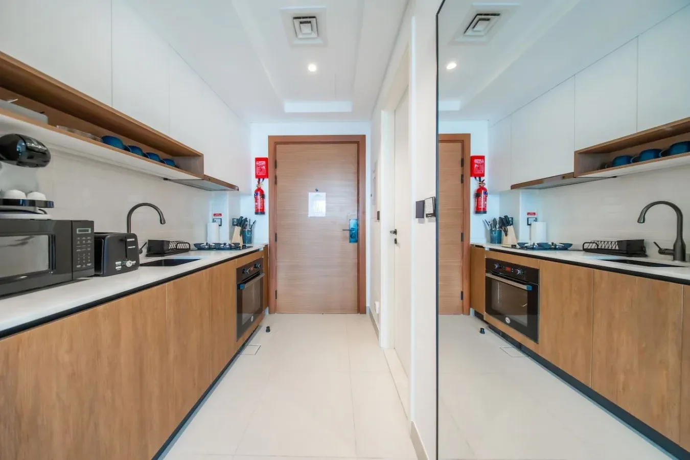 Una cocina compacta con gabinetes de madera, electrodomésticos sobre la encimera y una puerta al fondo.