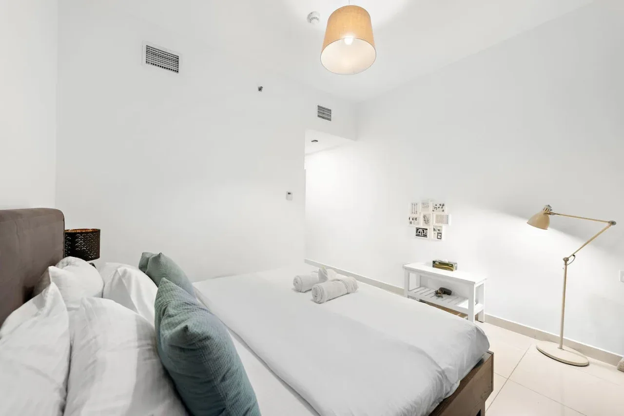 Un dormitorio luminoso con ropa de cama blanca y una mesita de noche.