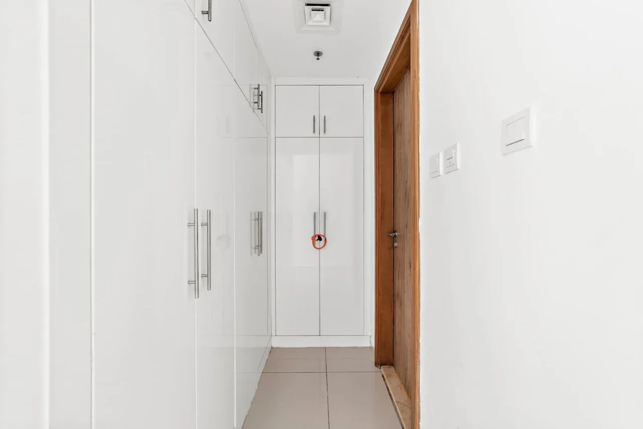 Un pasillo luminoso con armarios blancos empotrados y una puerta de madera.
