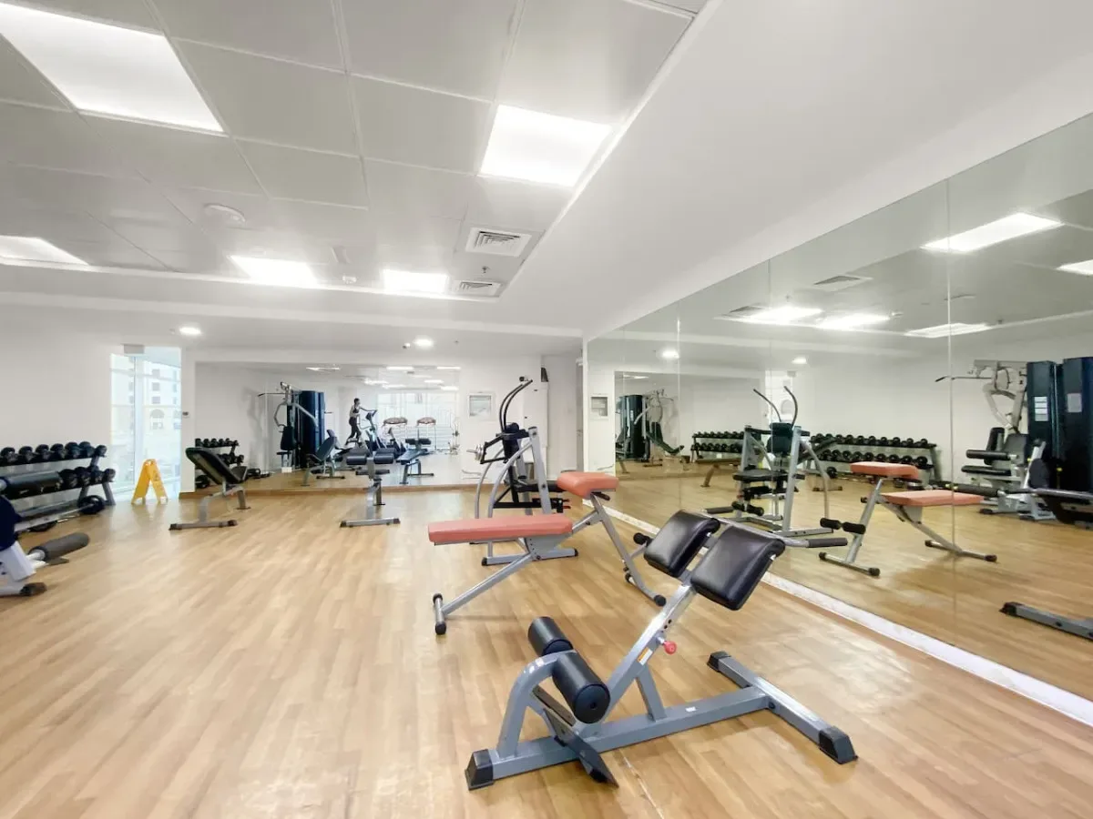 Un gimnasio con máquinas de ejercicio y bancos de pesas junto a paredes con espejos.