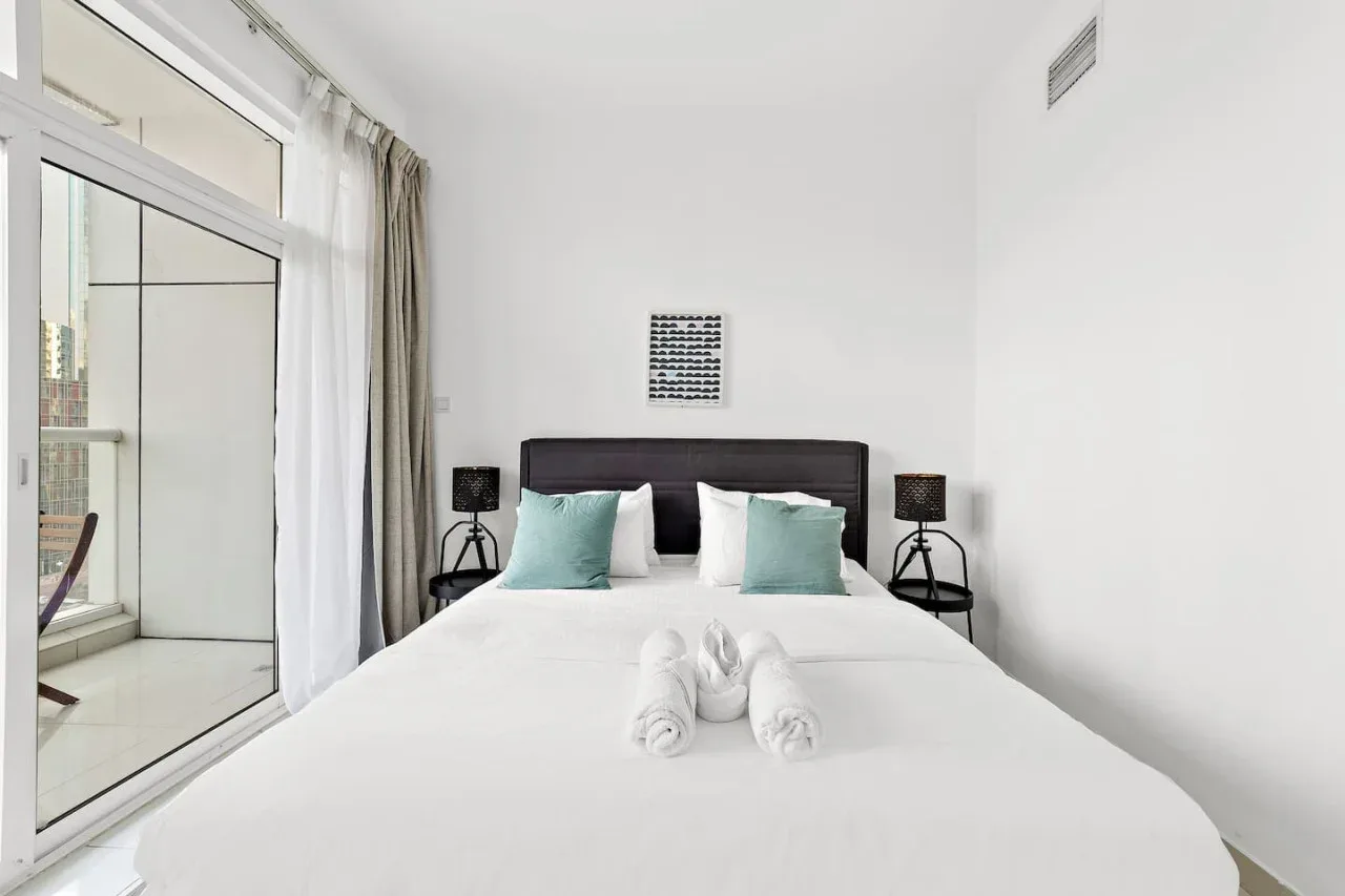 Un dormitorio luminoso con una cama bien tendida y puertas de cristal.