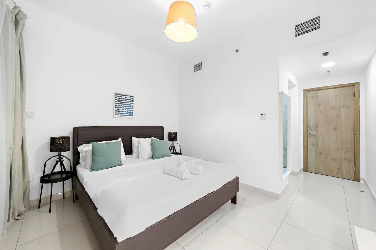 Un dormitorio luminoso con una cama doble y una puerta que da al pasillo.