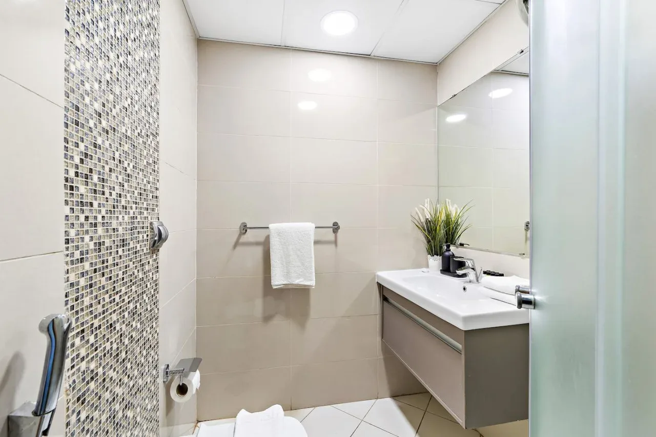 Un baño con lavabo, espejo y zona de ducha con azulejos.