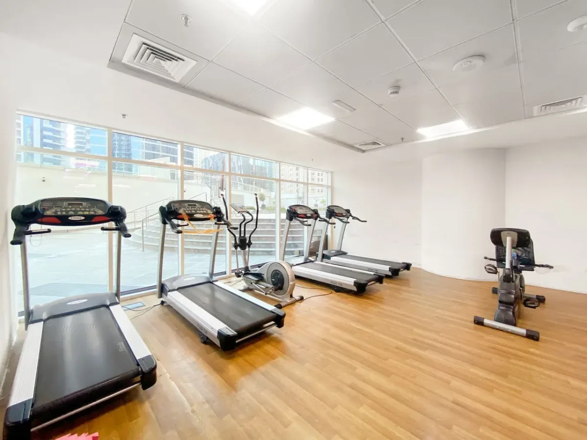 Un gimnasio luminoso con cintas de correr y equipo de ejercicio junto a grandes ventanas.