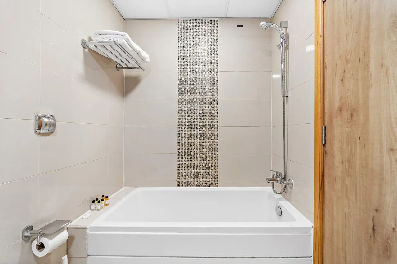 Baño con bañera, ducha de pared y un detalle de azulejos de mosaico.