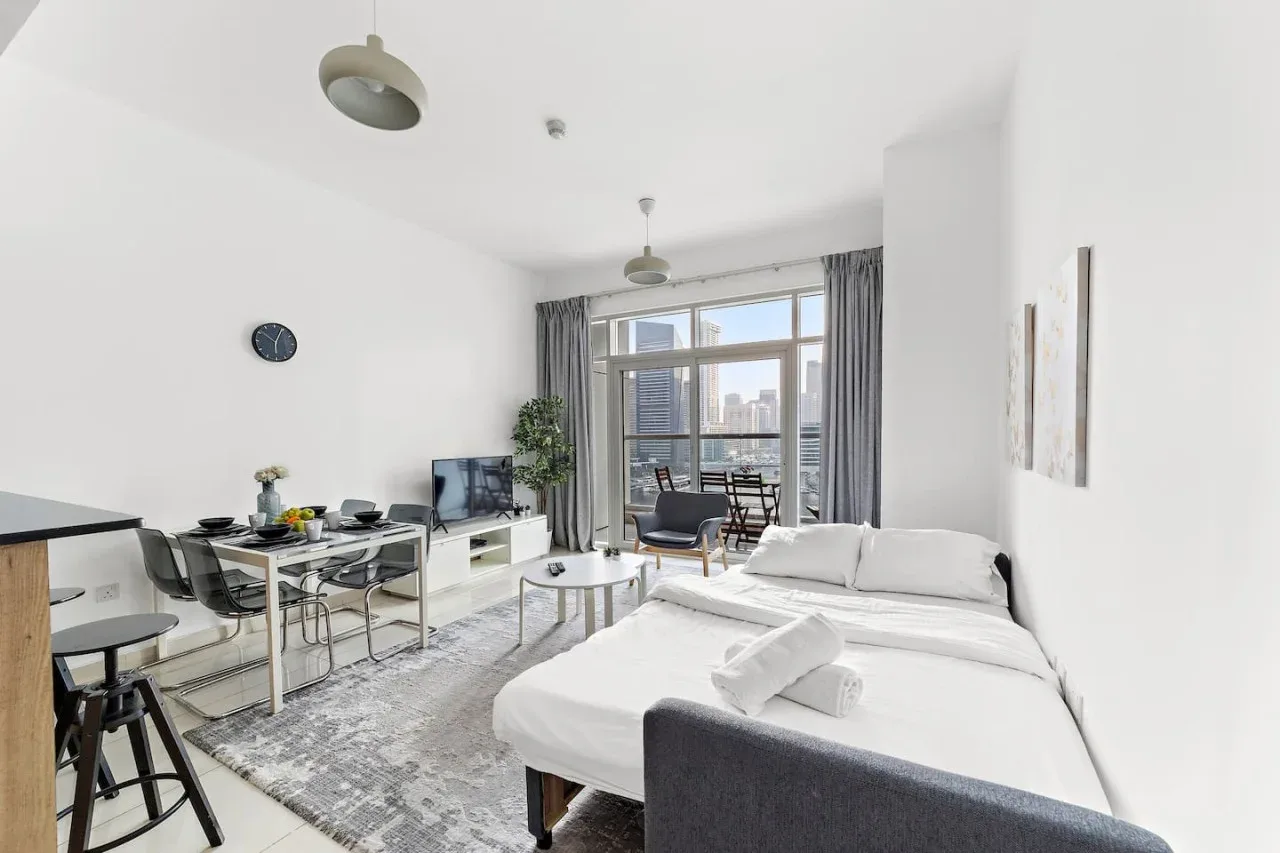 Una habitación tipo estudio luminosa con cama, zona de comedor y grandes ventanas.