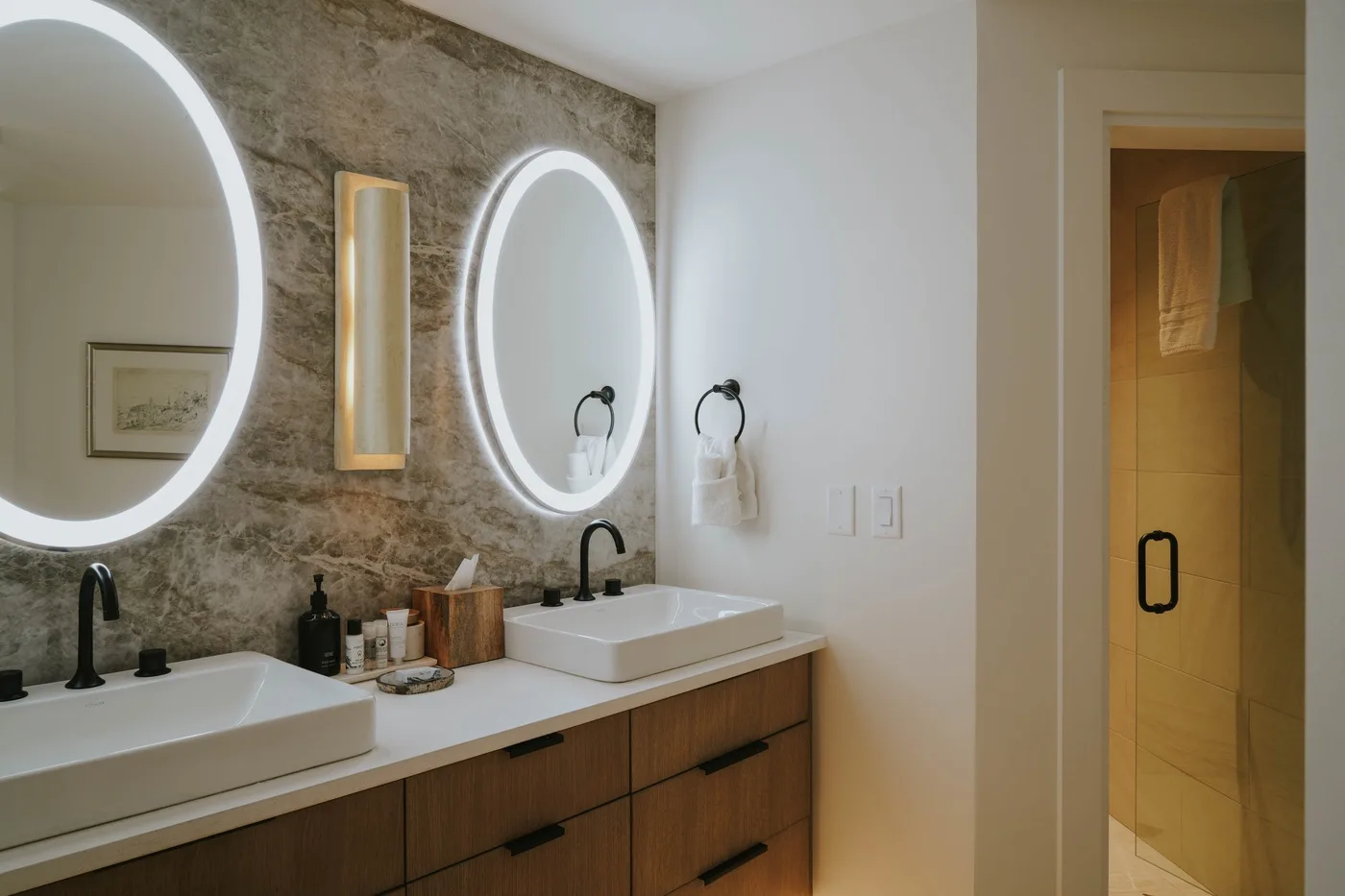 A bathroom vanity with illuminated mirrors and a shower doorway.