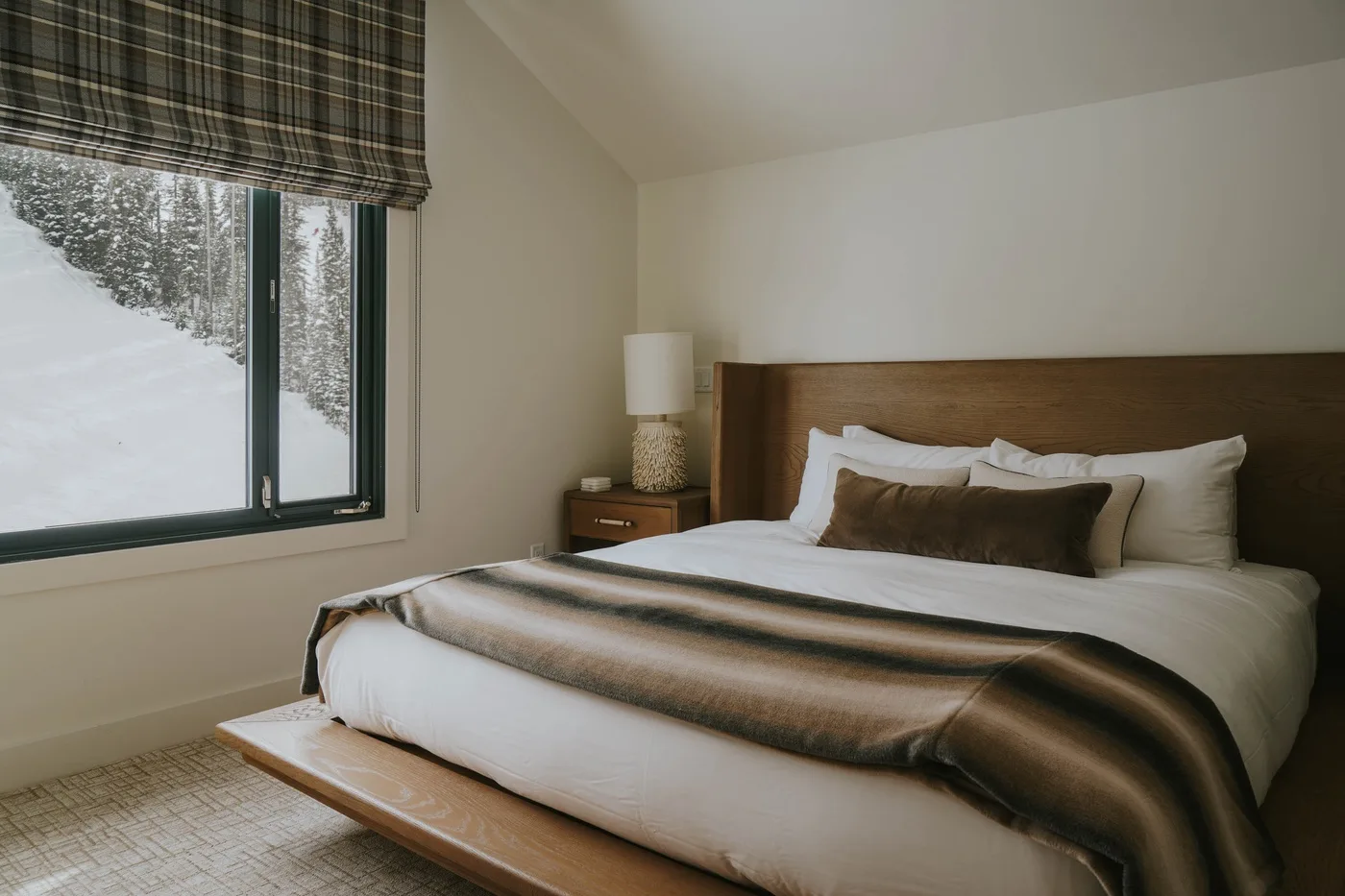 A bedroom with a neatly made bed and a large window overlooking snowy trees.