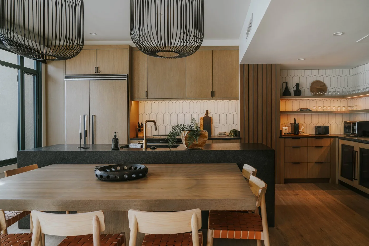 A modern kitchen and dining area with a wooden table and pendant lights.
