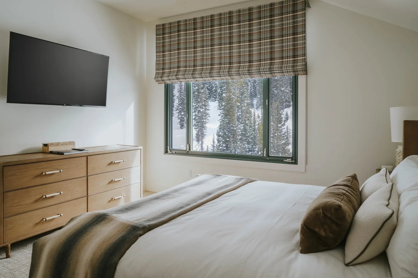 A bedroom with a bed beneath a window overlooking snow-covered trees.