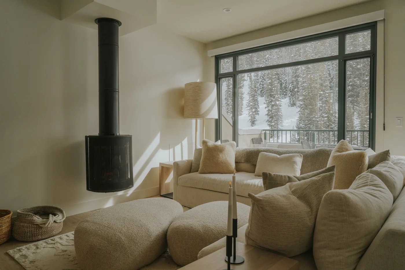 A living room with cushioned seating beside a large window overlooking snowy trees.