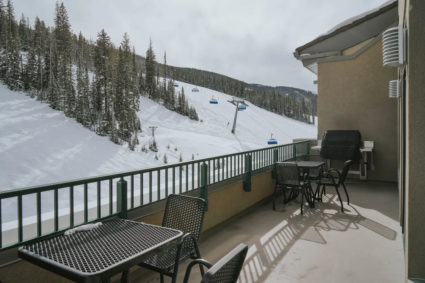 A patio with outdoor seating overlooks a snowy ski slope and evergreen trees.
