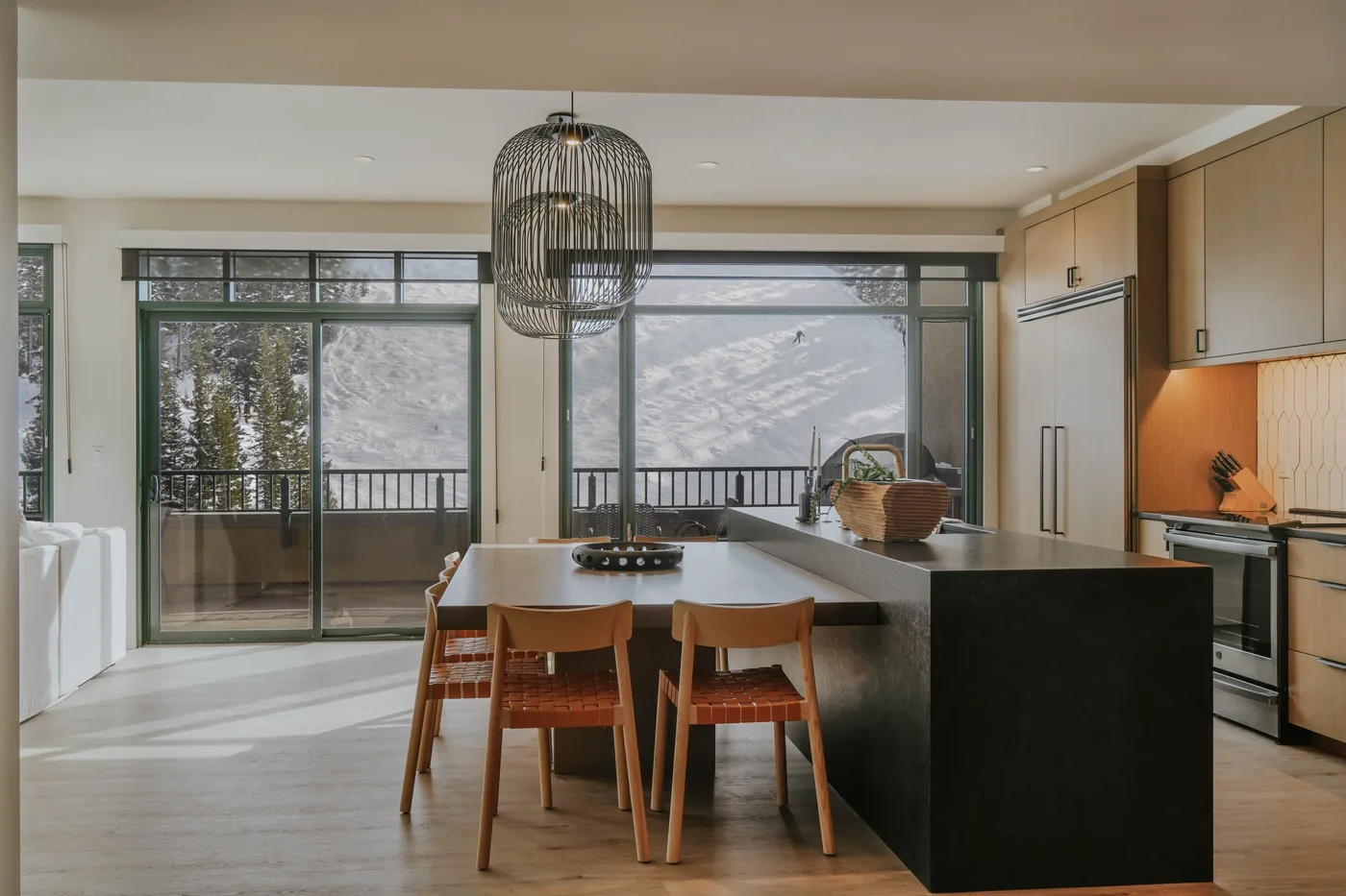 A modern kitchen and dining area opens onto a balcony with mountain views.