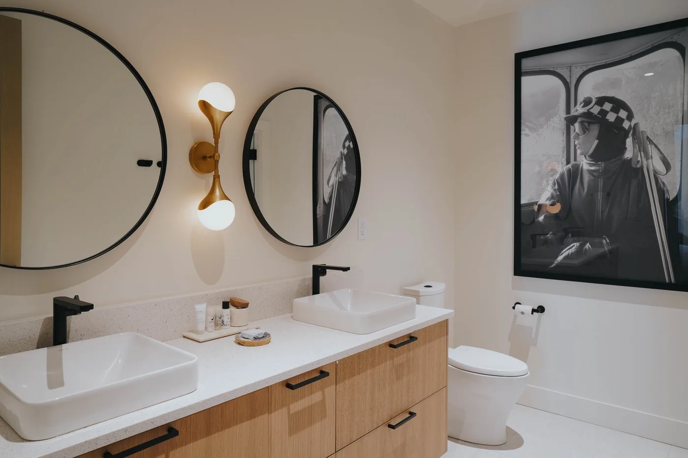 A modern bathroom with a double vanity, round mirrors, and framed wall art.