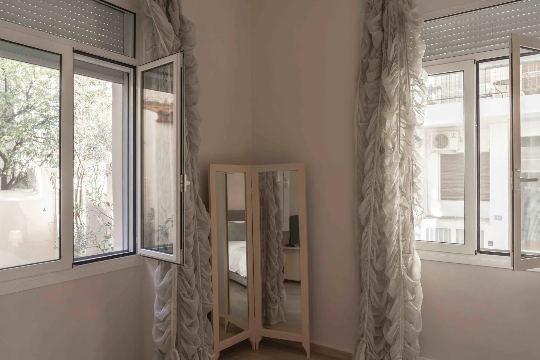 Una habitación luminosa tiene dos ventanas y un espejo de pie entre ellas.