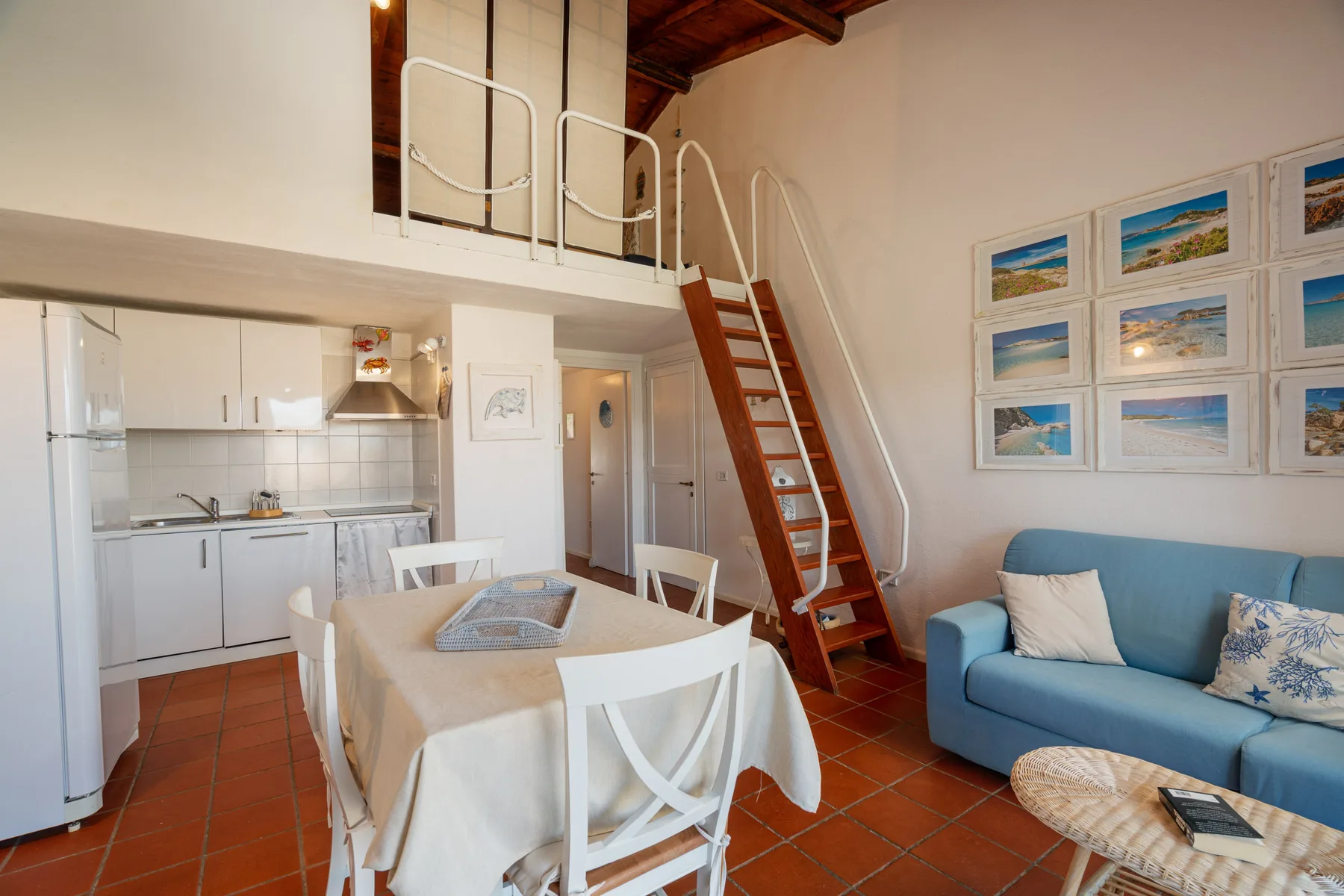 Comedor junto a una cocina compacta, con un sofá azul bajo cuadros enmarcados.