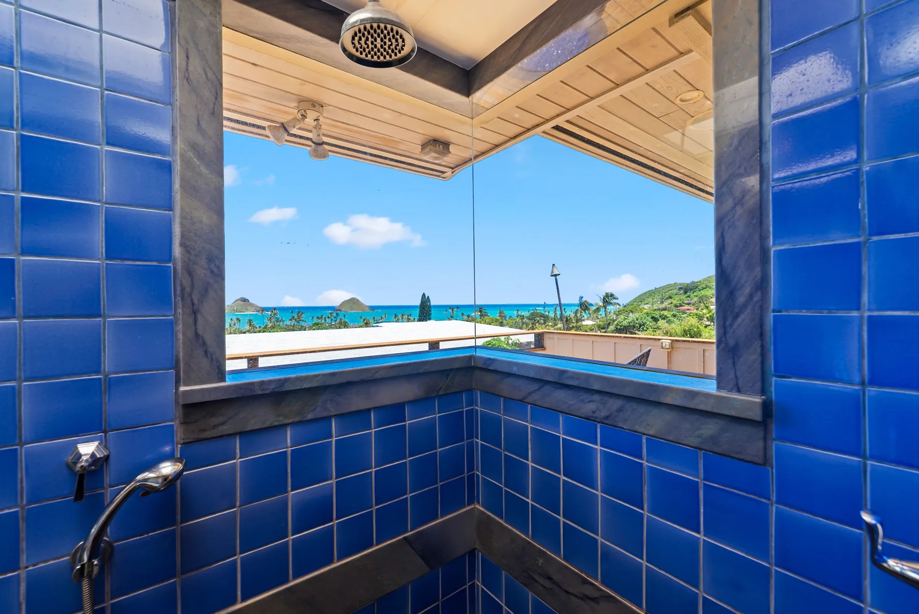 Una zona de ducha al aire libre con paredes de azulejos azules da al océano.