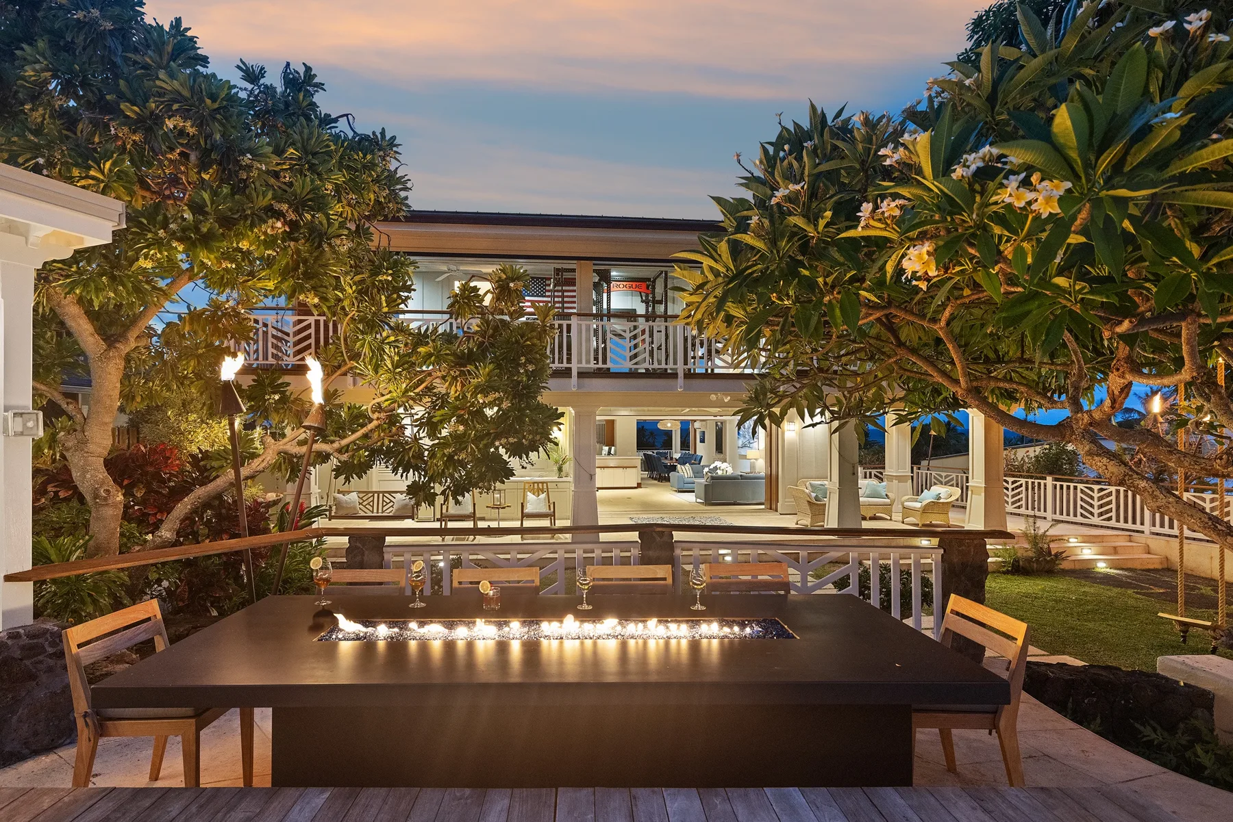Una casa moderna de dos plantas se alza detrás de una mesa de comedor al aire libre y un jardín.