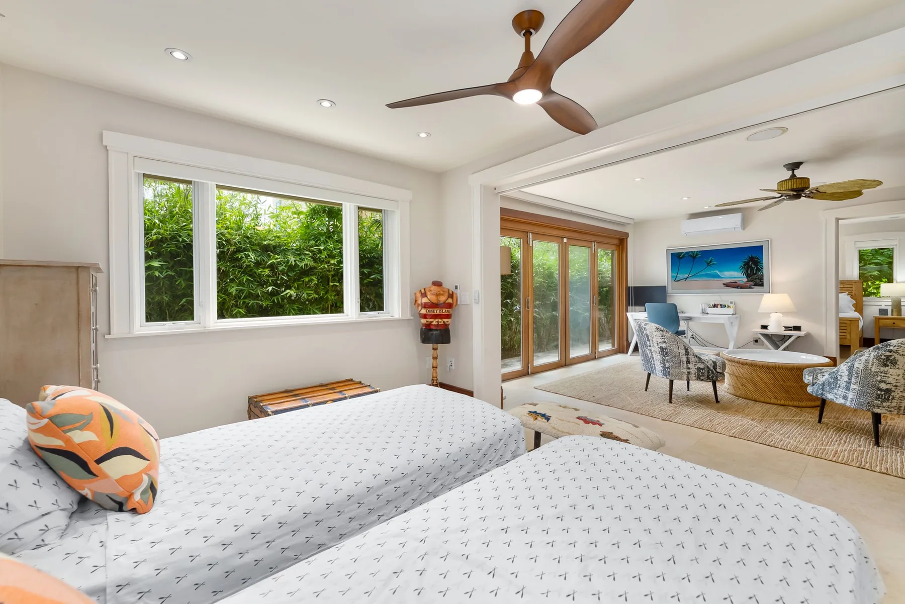 Un dormitorio con dos camas se abre a una zona de estar con grandes ventanas.