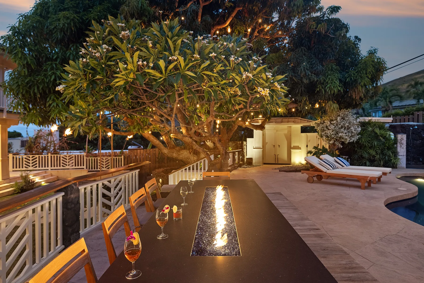 Un patio al aire libre con una mesa de comedor, asientos de descanso y un árbol grande.