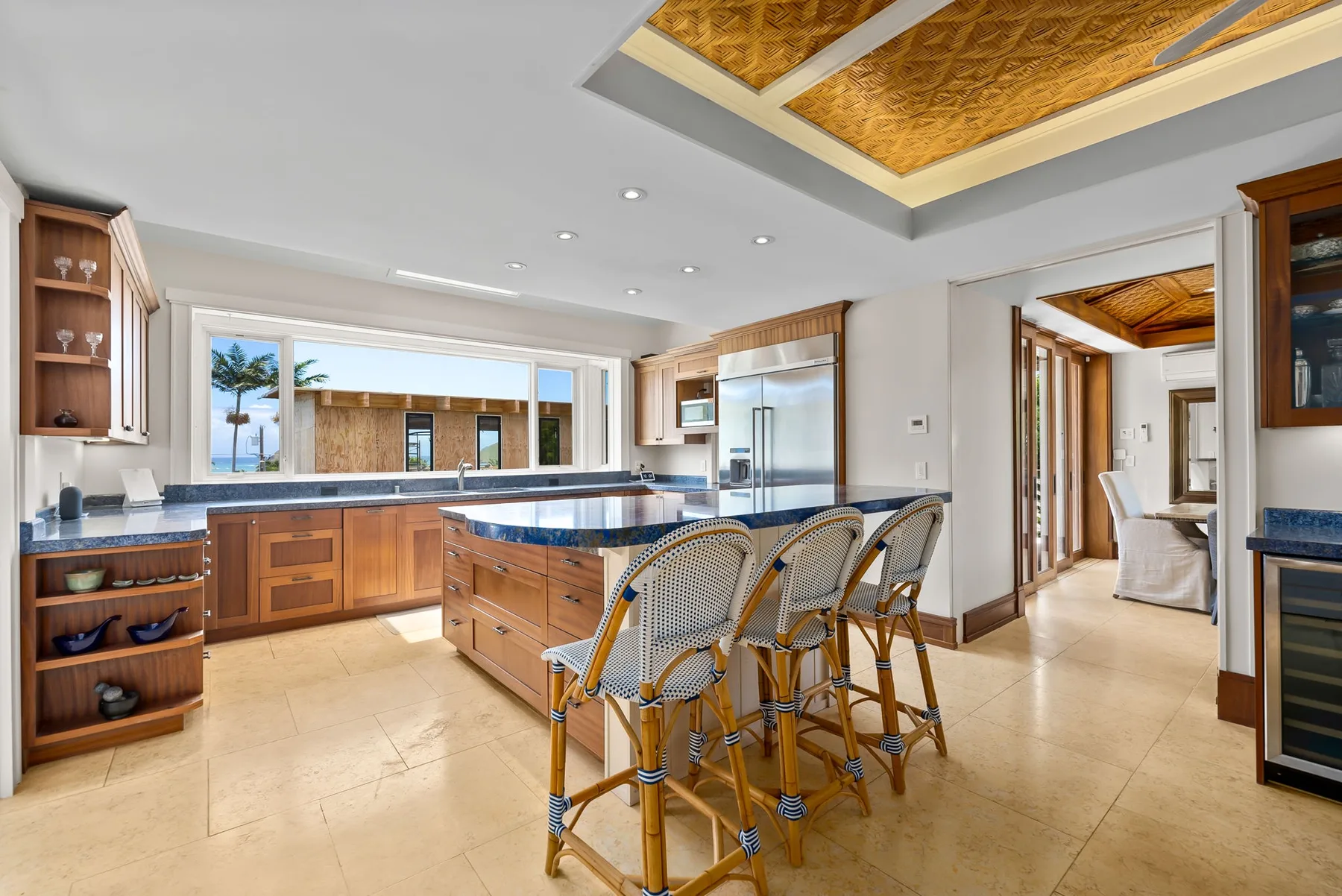 Una cocina luminosa con isla central, asientos de barra y ventanas grandes.