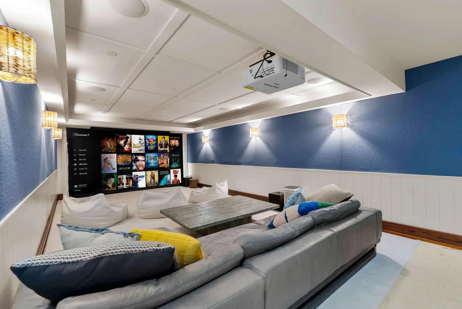 Una zona de estar orientada hacia una pantalla grande, con luces de pared y paredes azules.