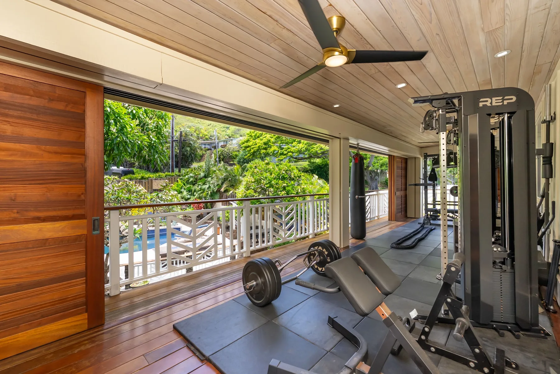 Un gimnasio con equipo de ejercicio junto a un balcón abierto con vistas a la vegetación.