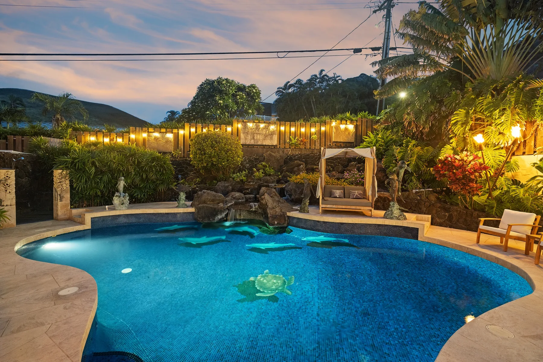 Una piscina está rodeada de plantas tropicales y asientos al anochecer.