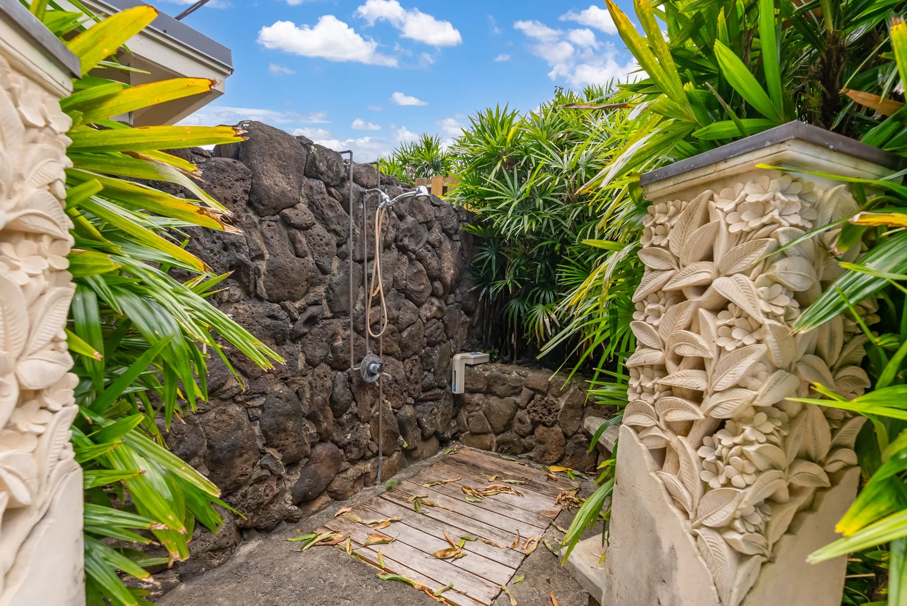 Una ducha al aire libre tiene una pared de piedra y abundante vegetación tropical.