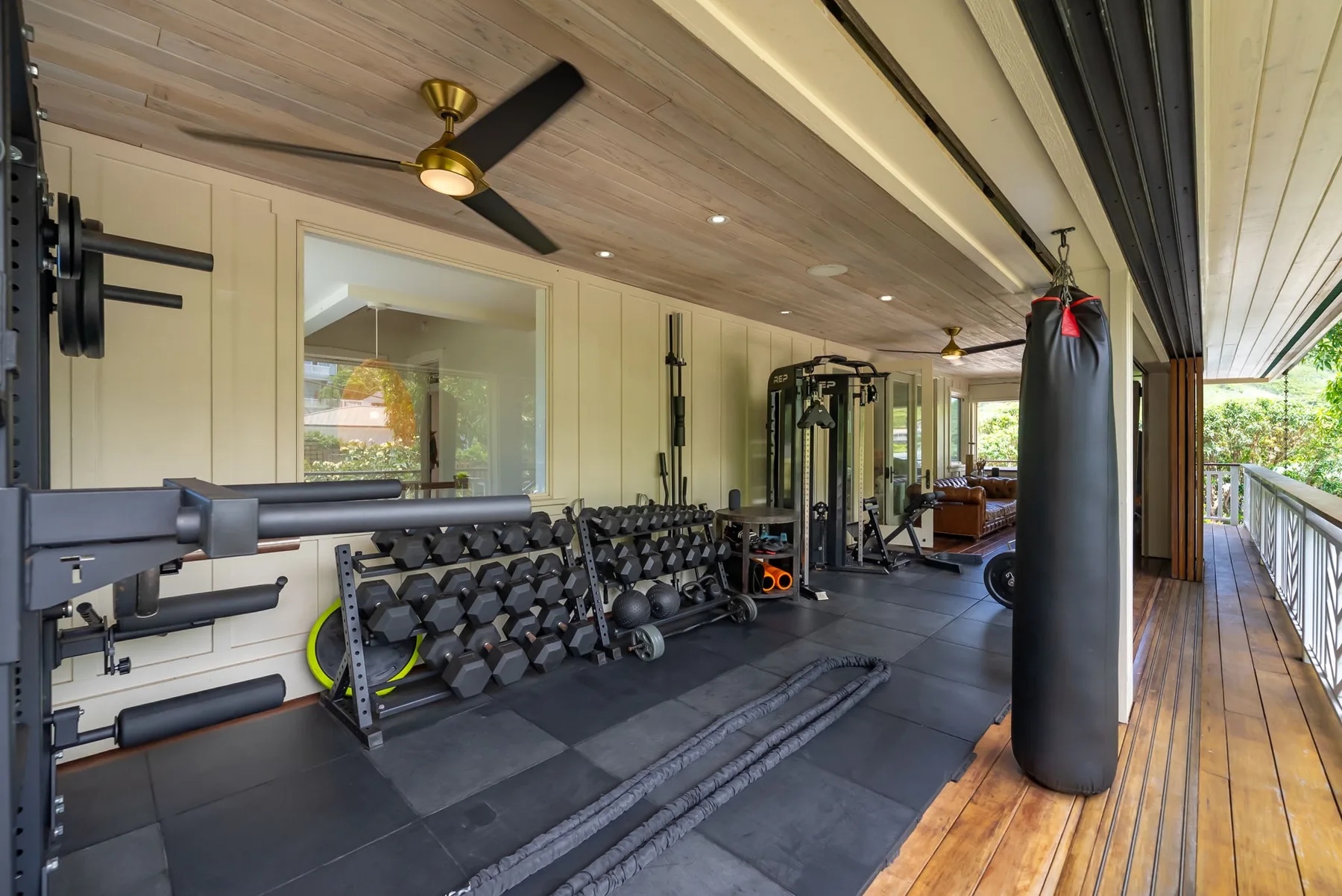 Una zona de gimnasio con pesas y un saco de boxeo junto a una terraza abierta.