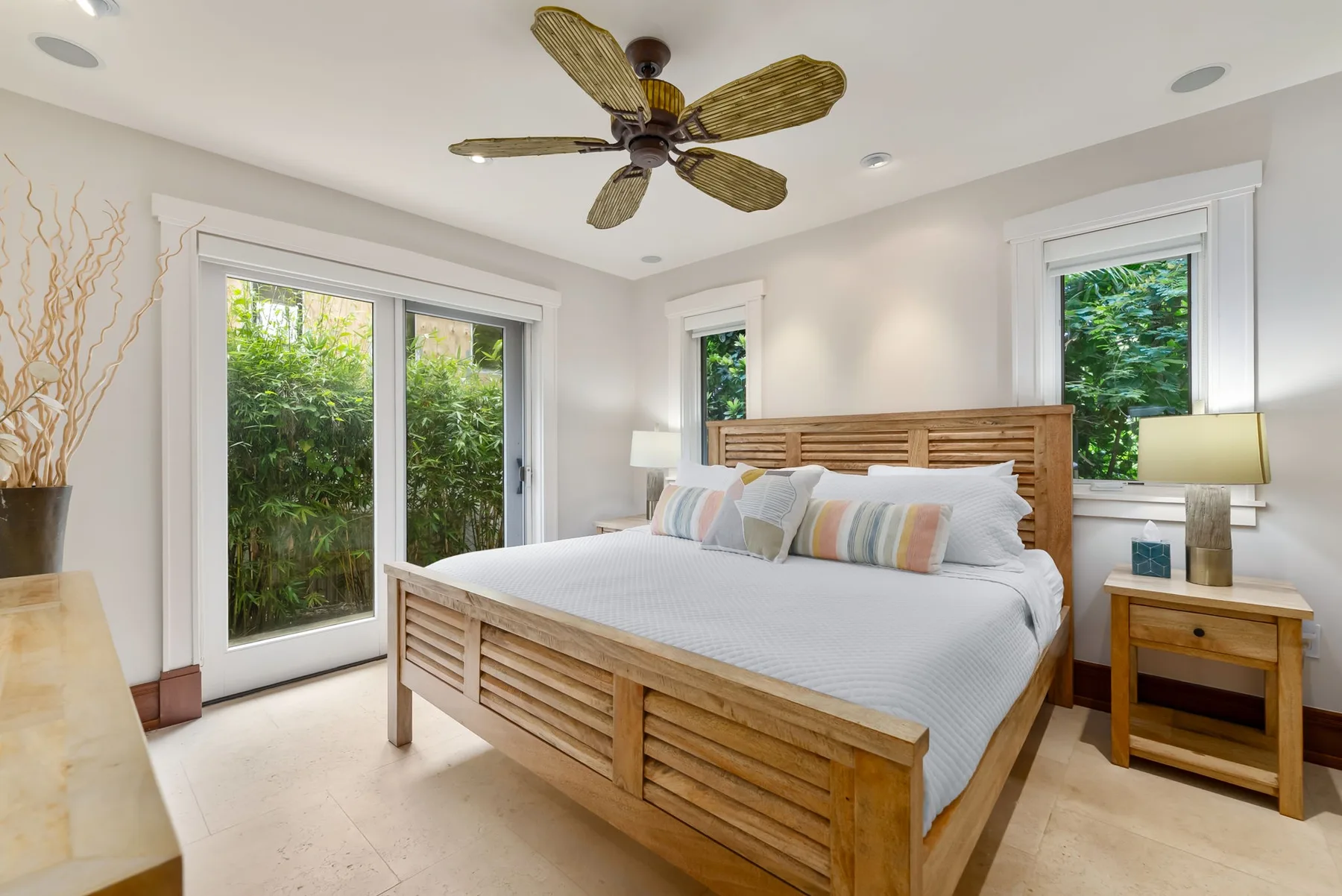 Un dormitorio luminoso con una cama de madera, ropa de cama clara y vistas frondosas por las ventanas.