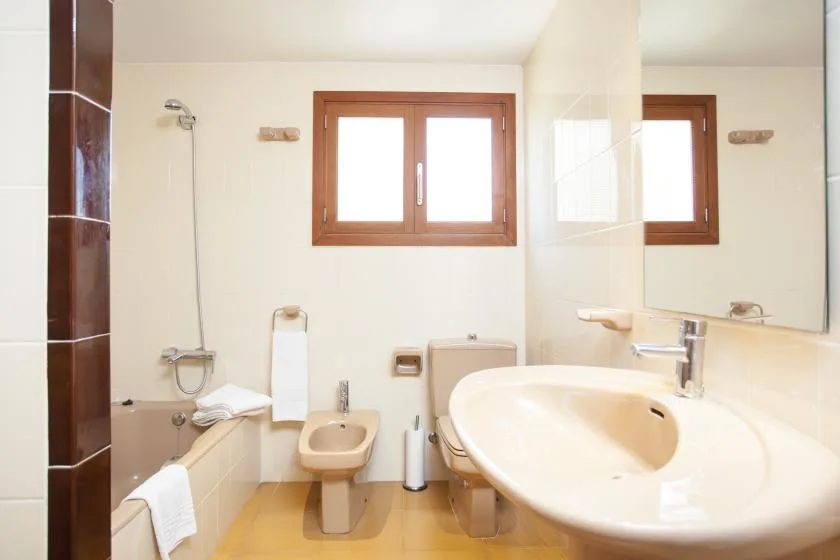 A bright bathroom with a bathtub, toilet, and wood-framed window.