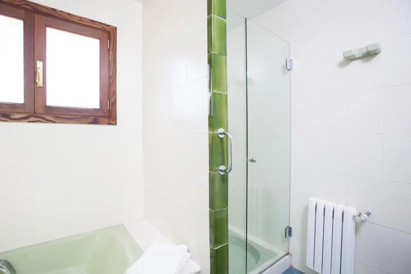 A tiled bathroom with a glass shower, a bathtub, and a window.