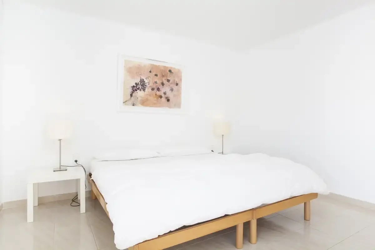 A bright bedroom with a bed beneath a small framed artwork.