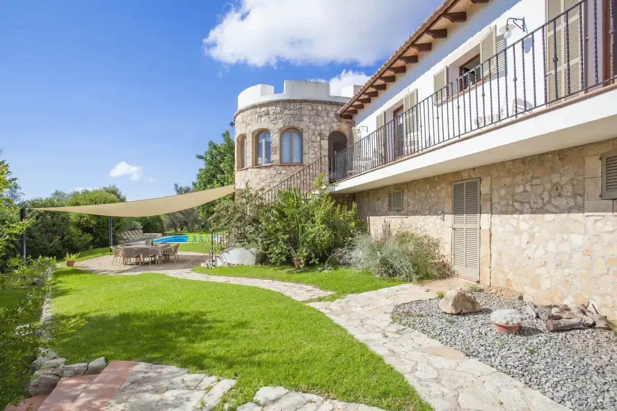 A stone house overlooks a garden with a lawn, patio, and shade canopy.