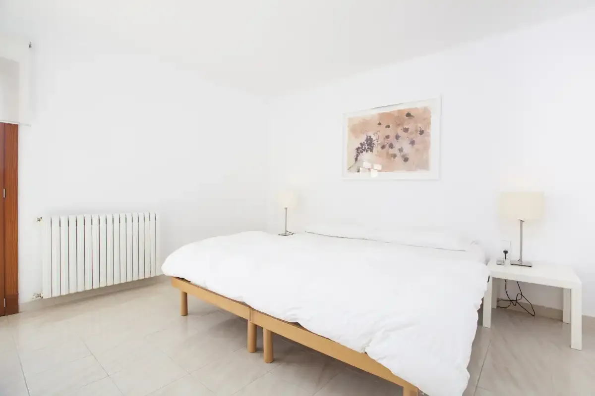 A bright bedroom with a bed, radiator, and bedside table.